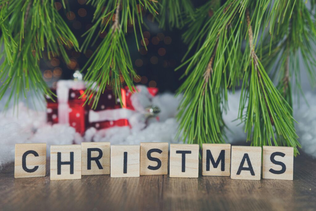 A festive Christmas setting featuring letter tiles spelling 'Christmas' amidst pine branches and gifts.