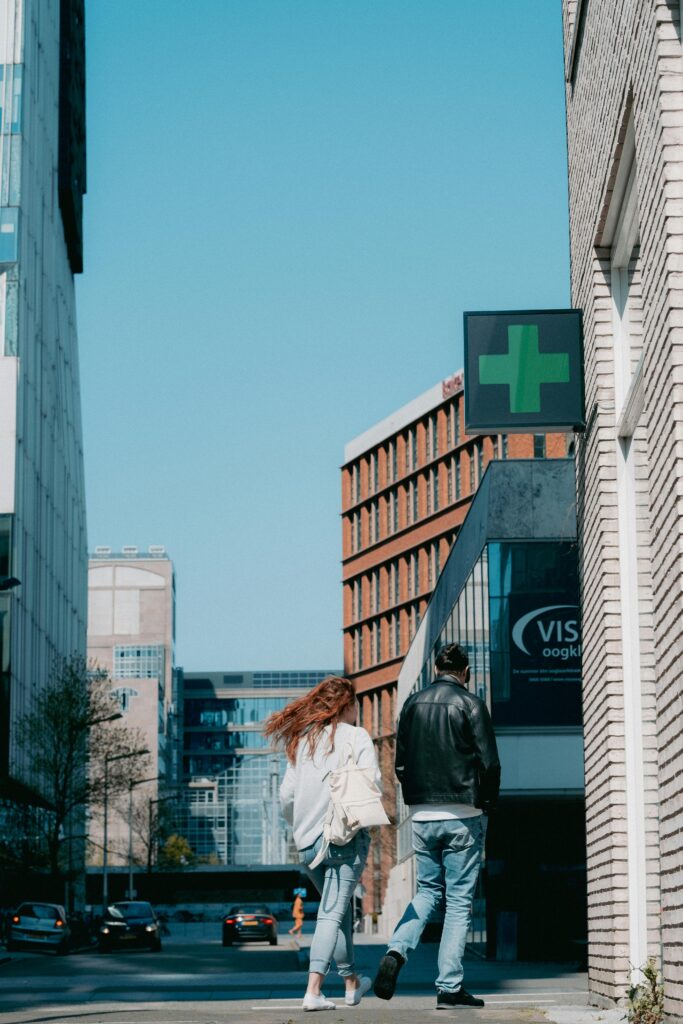 Man and woman walking in a modern urban area with buildings and sidewalk under a clear blue sky.