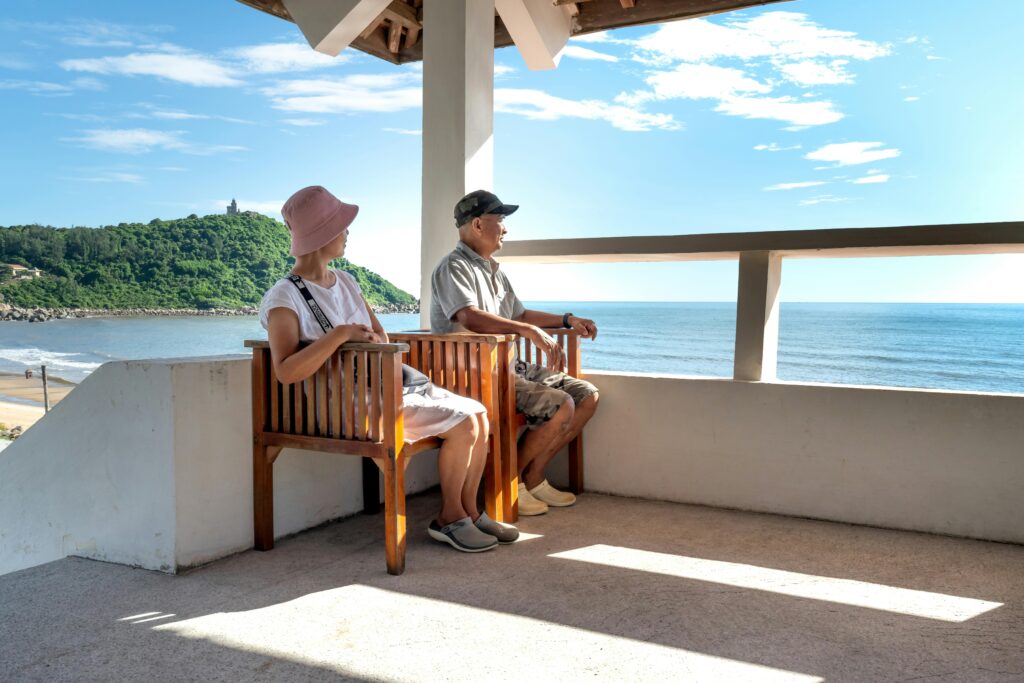 Senior couple sitting on balcony chairs, enjoying a relaxing ocean view in summer.