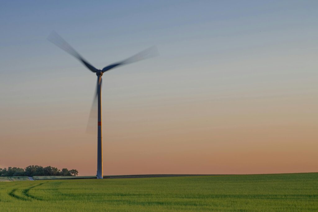 Electricity pole of windmill located farmland with green long meadow grass growing in countryside