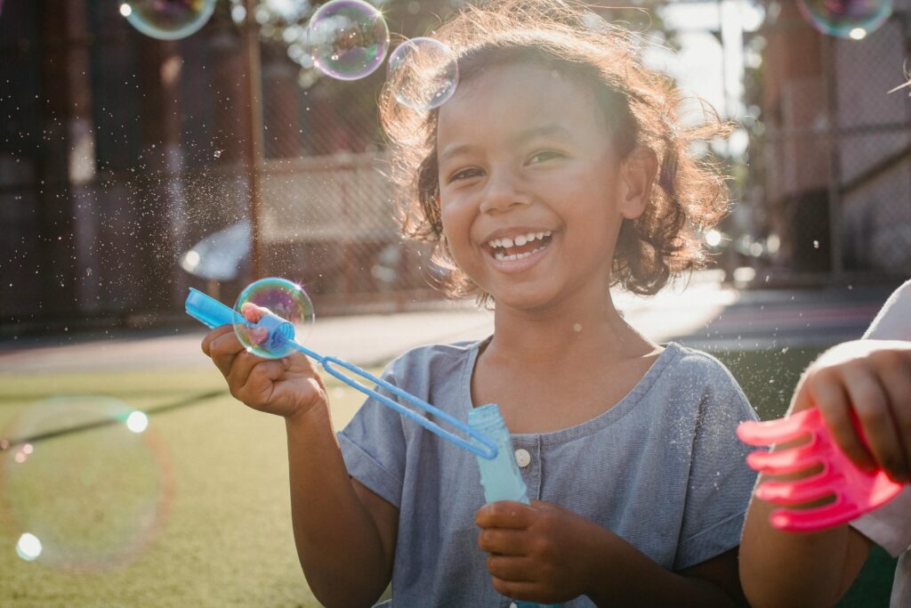 A cheerful young girl enjoys playing with soap bubbles outdoors on a sunny day.