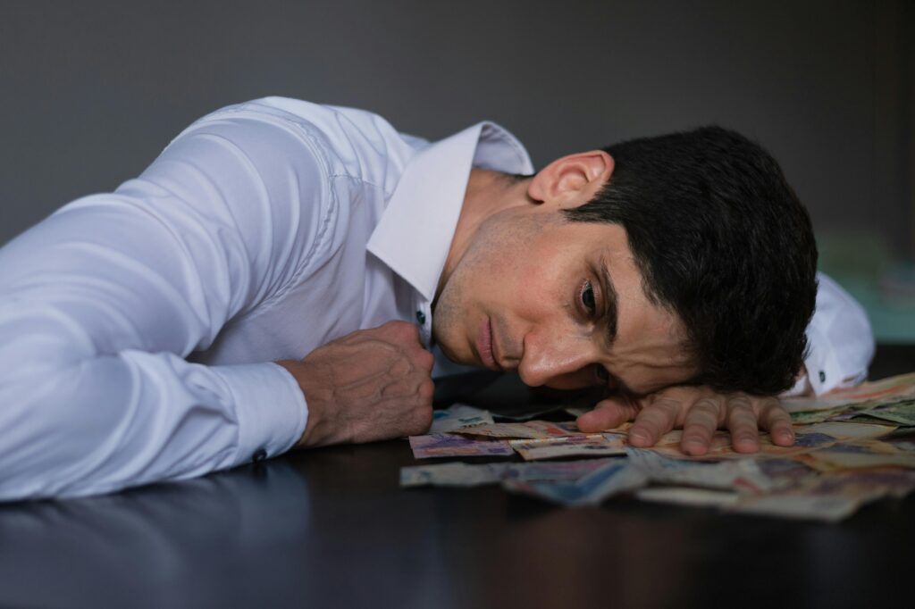 Adult man in white shirt resting on Argentine currency, showing financial stress.