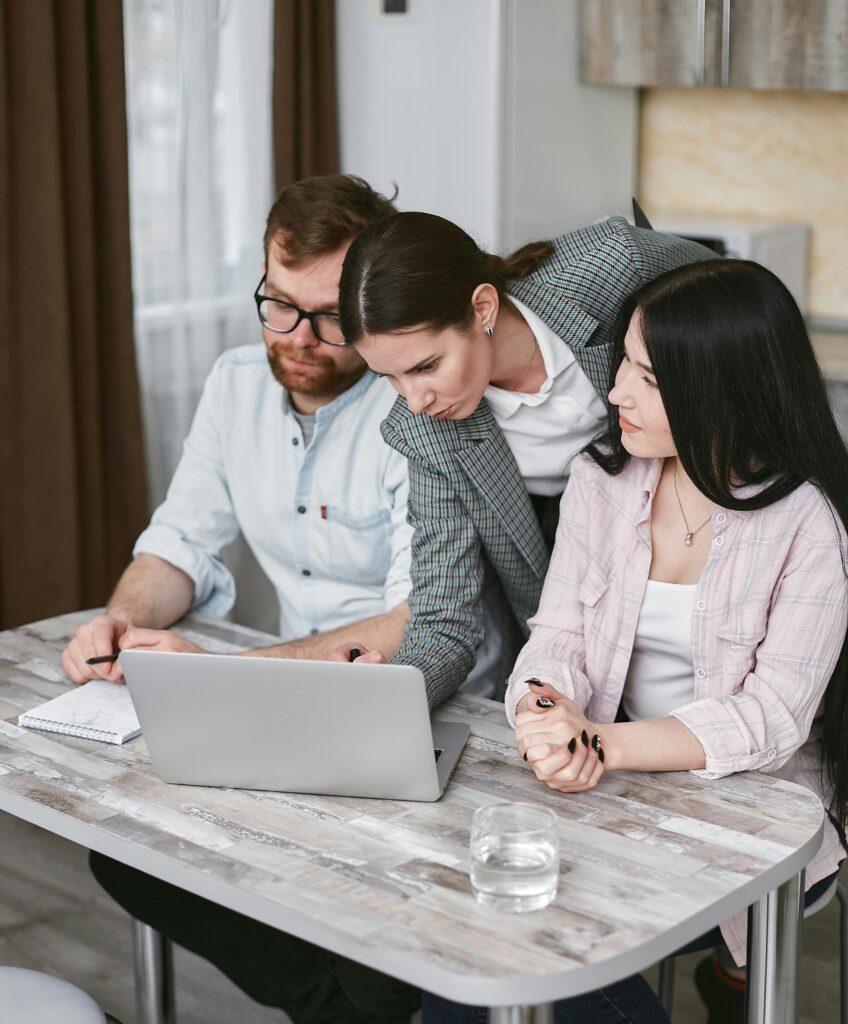 Three colleagues working together on a laptop, showcasing teamwork and collaboration in an office environment.
