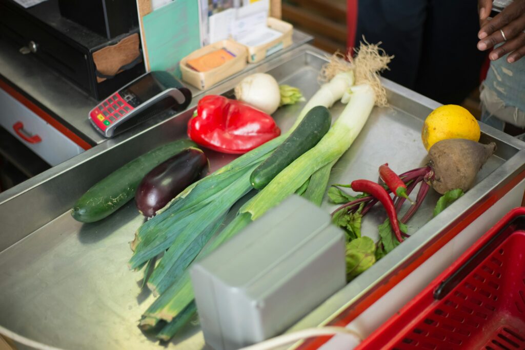 A selection of fresh vegetables on a stainless steel grocery checkout counter.